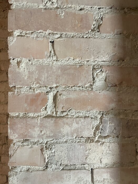 Tegelvägg med synliga fogar och ojämna murbrukslagningar i behov av reparation och renovering för att återställa 1920-talsutseendet.