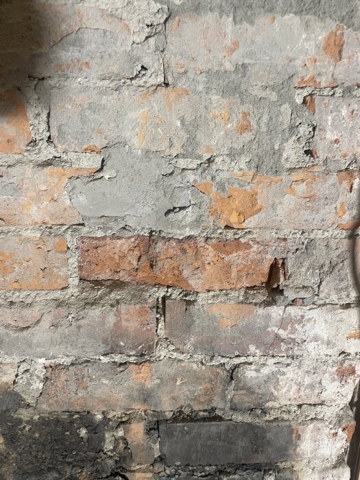 Murstock med synliga tegelfogar, skadad murbruk och cementfyllningar. Några stenar är naggade i kanten. Renoveringsbehov syns tydligt.