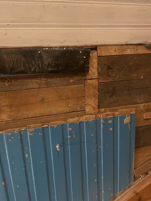 Svart plast syns mellan gipsskiva och träplank på innervägg, delvis täckt av blått träpanel.