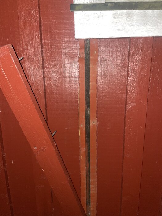 Röd träpanel med borttagen bräda visar svart masonit bakom.