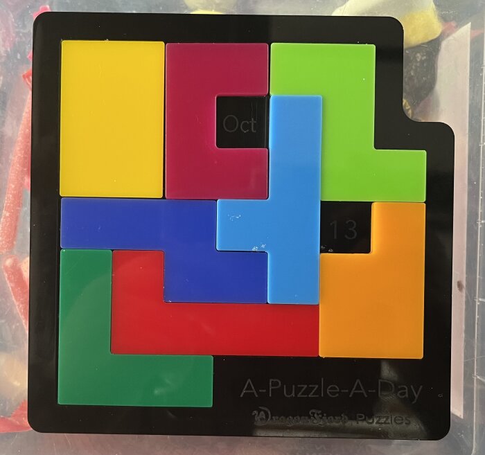 Flerfärgat pussel med bitar i rött, gult, blått och grönt i en svart ram. Texter "Oct" och "13" syns på bitarna.