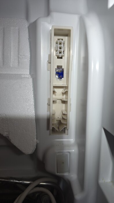 Inre delen av en Electrolux-fryss, visar en kontakt med flera terminaler och en blå säkring eller komponent i botten av urtaget.
