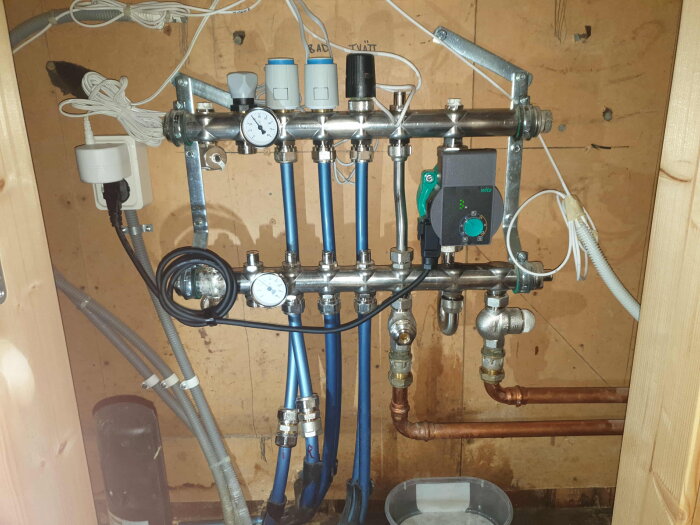 Vattenrörsystem med ventil och nyinstallerad pump, slangar och mätare inuti ett trångt skåp; en del av ett hemrenoveringsprojekt.