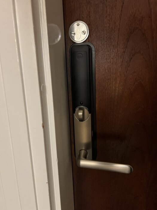 Smartlås, Yale Doorman L3S, installerat på en trädörr från 1969, med silverfärgat handtag och en rund platta ovanför.