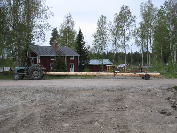 Traktor transporterar långt timmer på landsväg, enkel lantlig omgivning.
