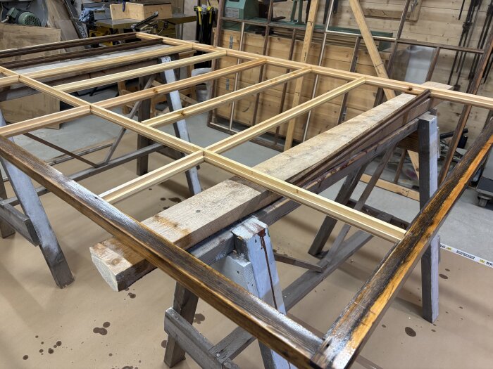 Träramar placerade på bockar i en verkstad, förberedelser för träbearbetning eller målning.