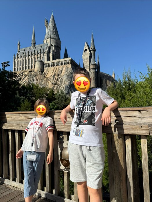 Barn framför en modell av ett magiskt slott med blå himmel i bakgrunden på en temapark.