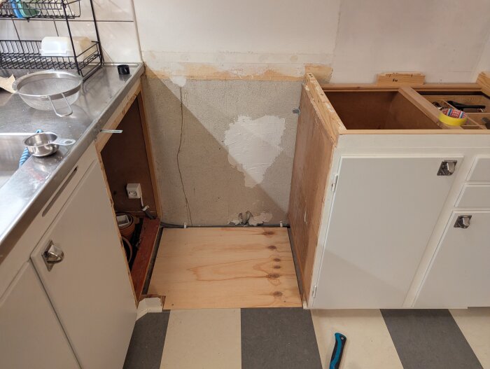 Kök under renovering, diskbänken är borttagen och ett nytt plywoodgolv är installerat i området där en diskmaskin ska placeras.