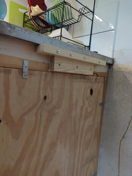 Trästruktur under diskbänk med skruvar och stödkonstruktion för bänkskiva, diskställ synligt ovanför.