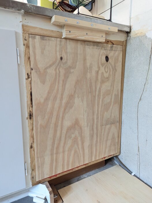 Träkonstruktion under diskbänk med ny kant och igensatt hål mot underskåpet, synliga skruvar och fogmassa för tätning.