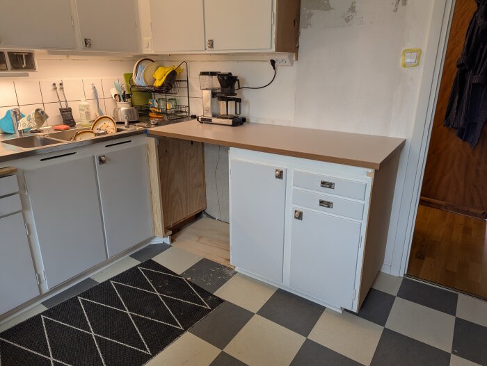 Nyinstallerade bänkskivor i ett kök med vita skåp och svartvit rutigt golv, klart för att fästas ordentligt.