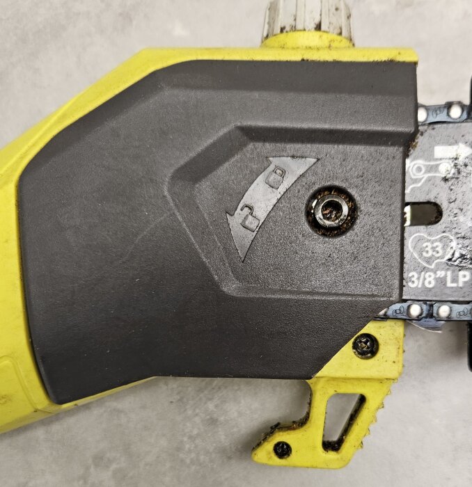 En närbild av en del av en motorsåg där en skruv håller fast kedjespännaren, med justeringsinstruktioner visade på det svarta höljet.