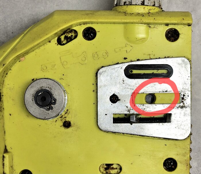 Gult verktyg med en metallskruv inringad i rött, del av en mekanism för kedjespänning, sedd ovanifrån.