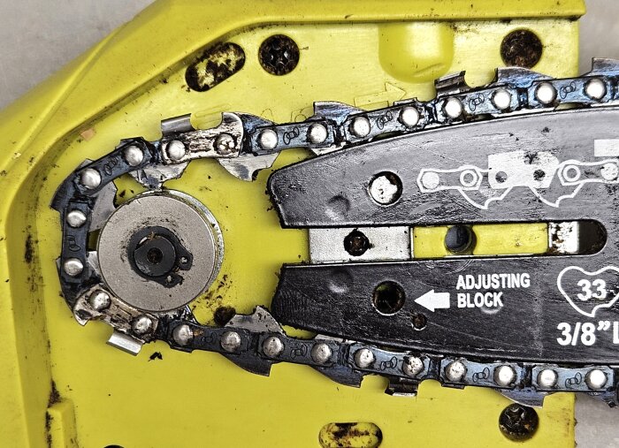 Bild på en kedjesåg med kedjespännare, där en skruv och en justeringsanordning syns tydligt på den gula höljet.