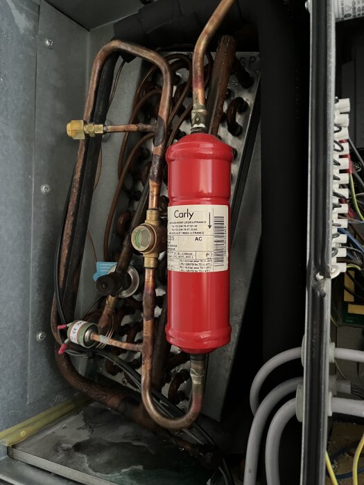 Rörsystem och behållare inuti ett öppet skåp, med en röd TLE-ventil märkt "Carly" synlig i centrum.