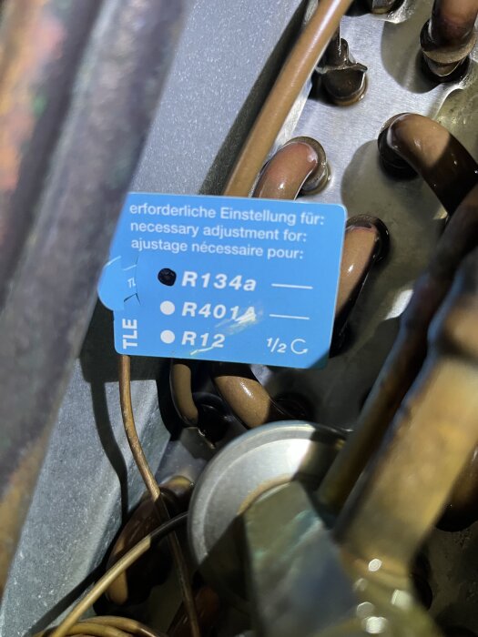 Närbild på en TLE-ventil med en blå etikett som visar justeringsinställningar för olika kylmedier, omgiven av kopparrör.