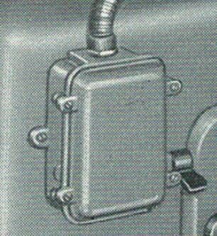 Gammalt motorskyddsfodral i metall monterat på vägg, med anslutande kabel upptill. Används i restaurering av maskiner med asynkronmotor.