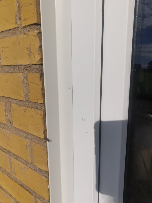 Vitt fönsterbleck på tegelvägg under solljus.