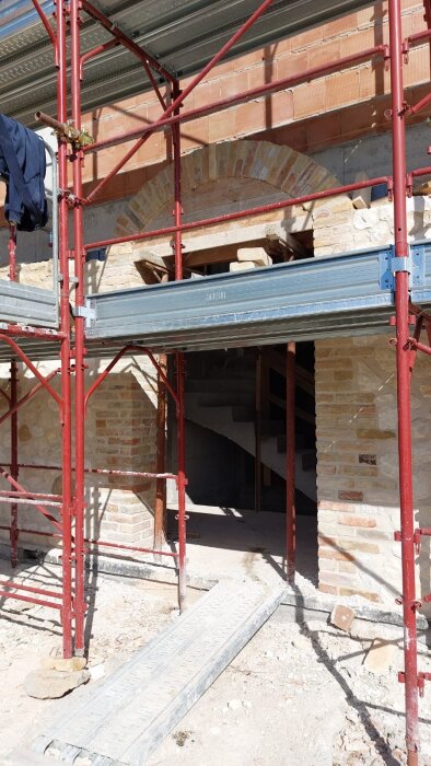 Byggnadsställningar framför en vägg under renovering med synliga tegelsten och en ingång med trappa.