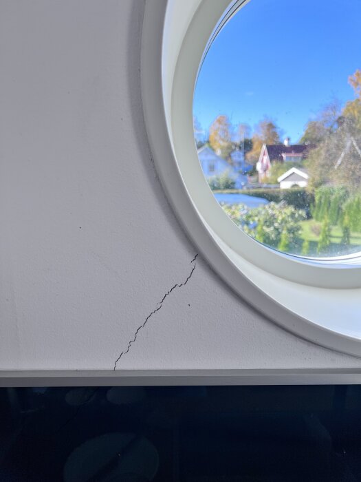 Spricka i vit vägg nära runt fönster med utsikt över trädgård och hus.