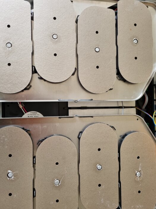 Induktionshäll isärskruvad med ovala delar och vit kontaktmassa synlig mellan glaset och magnetspolarna.