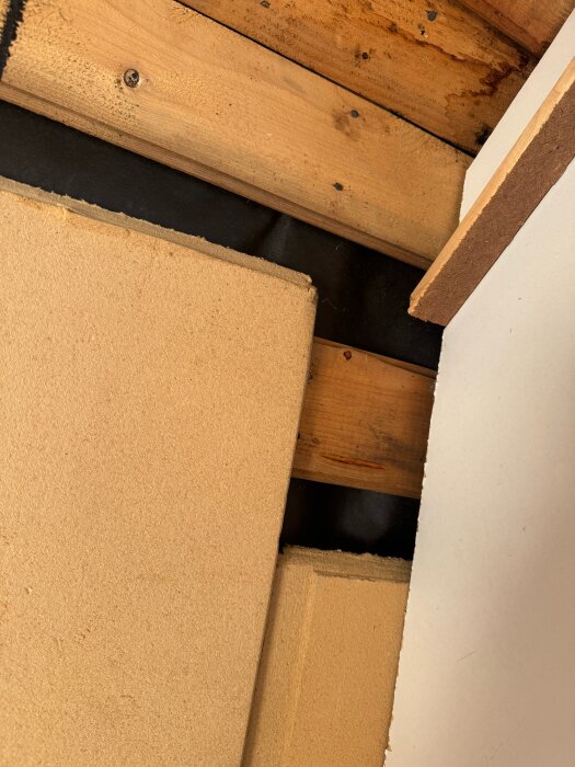 Delvis riven garderobsstruktur med träbalkar, isolering, spånskiva, och svart papp synlig i ett renoveringsprojekt från 60-tals hus.