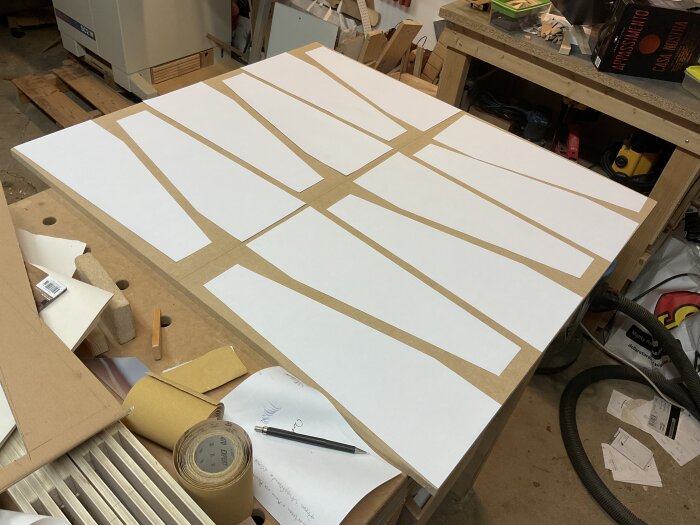 Pappersmallar utlagda på MDF-skiva för att planera utskärning av bitar till ben för soffbord; verktyg och material synliga i bakgrunden.