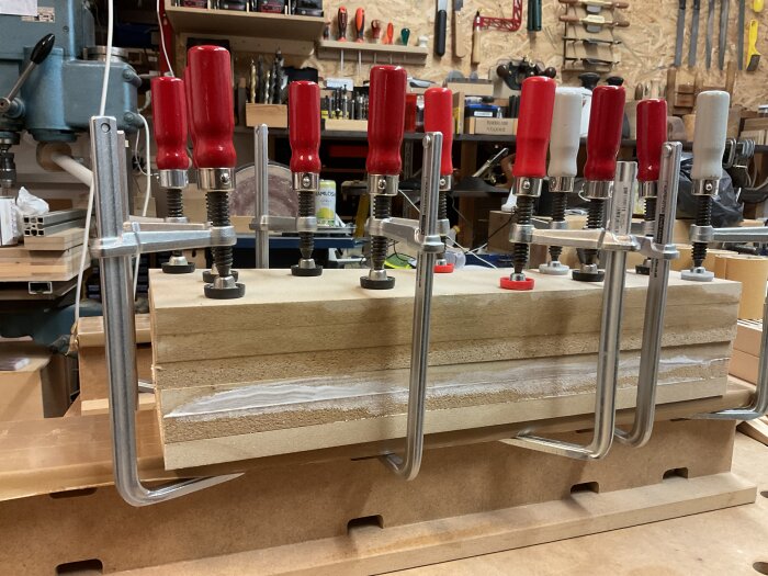 Träbitar av MDF limmas ihop med flera tvingar i en verkstad.