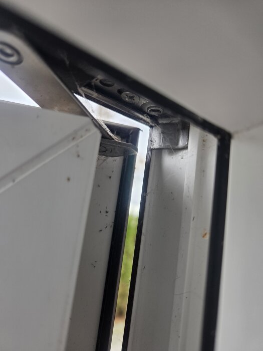 Närbild av PVC-fönster med öppning i övre hörnet där två metallstycken vid övre gångjärnet inte möts, vilket orsakar glipa.