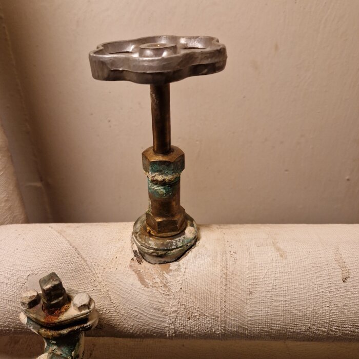 Gammal radiatorventil ovanpå ett rör, med metallvred monterat på en gängad stång, visar tecken på slitage och korrosion.