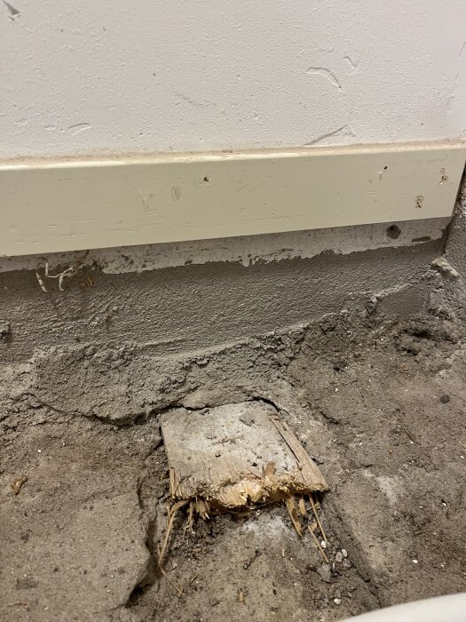 Gammalt träregel synlig under en vit källarvägg med avsliten yta och ojämnt golv i förgrunden. Potentiella byggproblem och renoveringsfrågor diskuteras.