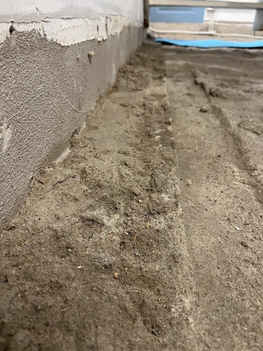 Ojämnt betonggolv nära en putsad vägg, med spår och ojämnheter i ytan, som en del av en diskussion om bygge och golvläggning.