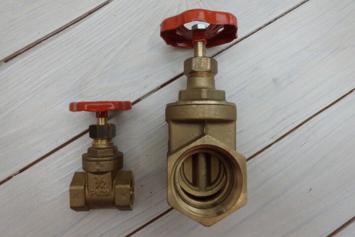 Två mässingsventiler med röda handtag på träplanka; en mindre 1/2 PN20 och en större, visas sida vid sida.