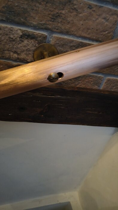 Träräcke med felborrat hål på en tegelvägg, synligt fäste och mörkt trä bakom. Problem med olika vägghöjd. Frågor om att täcka borrfelet.