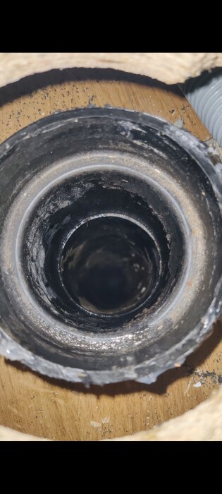 Svart avloppsrör som sticker upp från ett golv, sedd ovanifrån, med smuts och slitage.