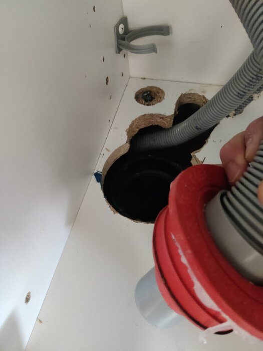 Röd muff/nippel vid avloppsrör i golvet, hand håller i grå slang, förbereder anslutning.