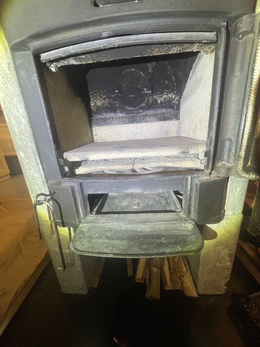 Öppen kamin med fastsatta vermikulitplattor och sotningsverktyg vid sidan.