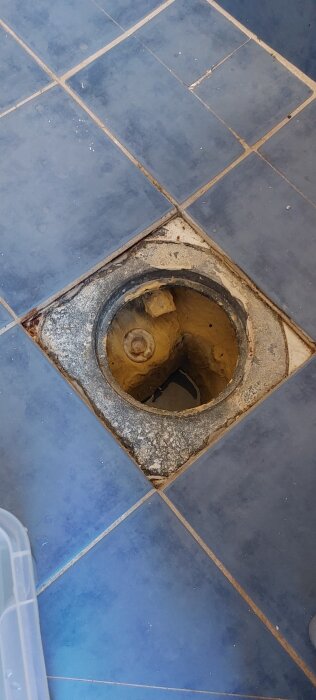 Golvbrunn med sned täckram, omgiven av blå keramikplattor, i en renoveringskontext där fukt och lösa plattor diskuteras.