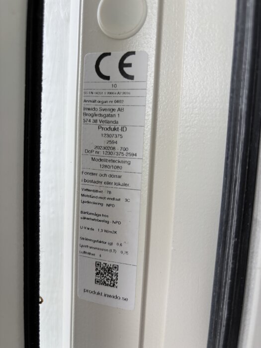 Etikett med CE-märke på fönsterkarmens gångjärnssida från Inwido Sverige AB, innehållande produkt-ID och tekniska specifikationer.
