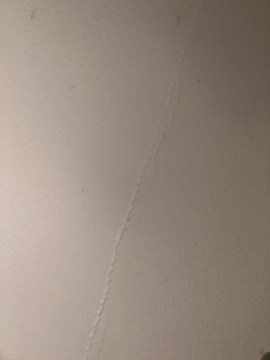 En närbild av en ojämn väggfog eller spricka i en ljus vägg, sedd i svagt ljus.