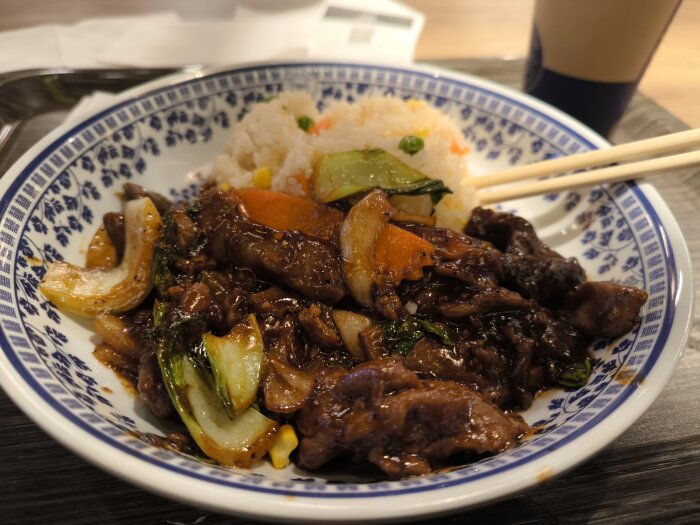 Pepperbiff med grönsaker och stekt ris på en tallrik, ätpinnar ovanpå, Chop Chop-restaurangmåltid.