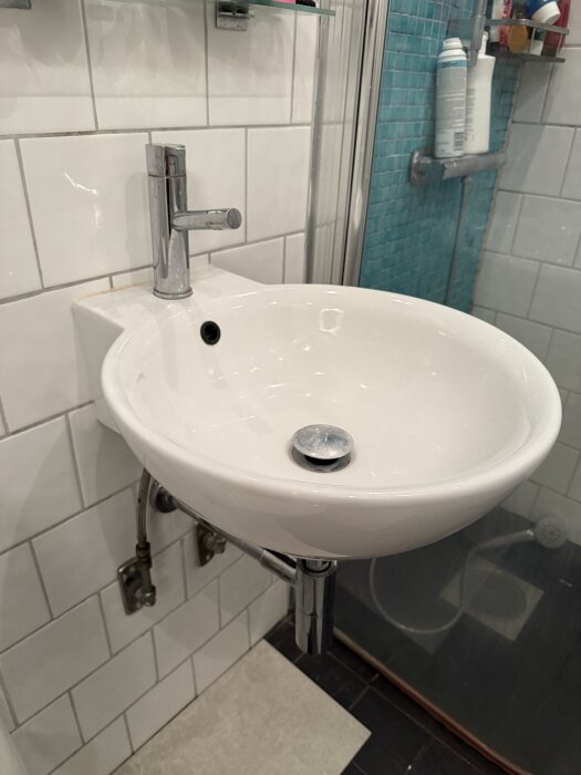 Smalt, runt tvättställ med vattenkran monterat på vitt, kaklat badrumsvägg.