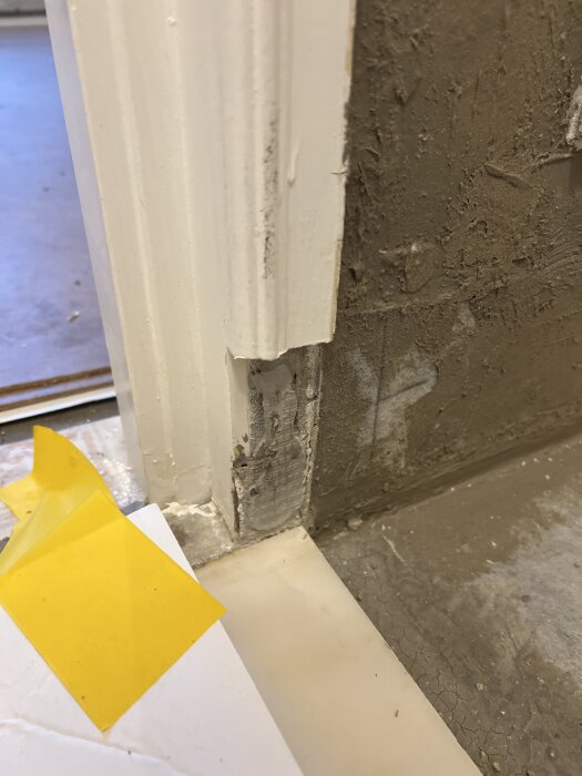 Tröskel och dörrkarm där tätskikt är under. Asymmetri syns mellan tröskel och vägg. Gult objekt bredvid visar på renoveringskontext.