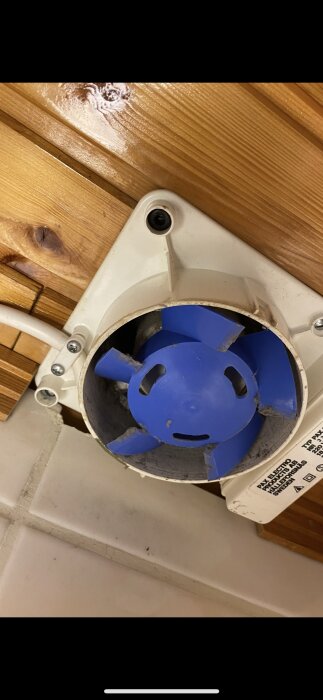 Takfläkt monterad i tak med träpanel och kaklad vägg.