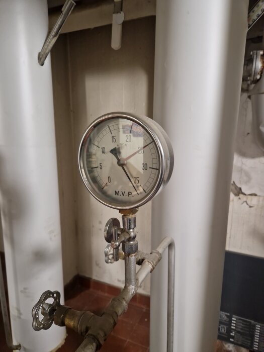 Manometer med tryck på cirka 4 bar, installerad på ett rörsystem i källarutrymme. Två stora vita rör syns i bakgrunden.