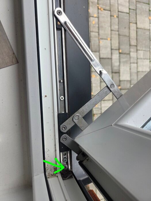 Fönsterkarm med öppen båge, ses från insidan. En grön pil pekar mot hörn med smuts och synlig skruv, en del av ett justerbart gångjärn syns.