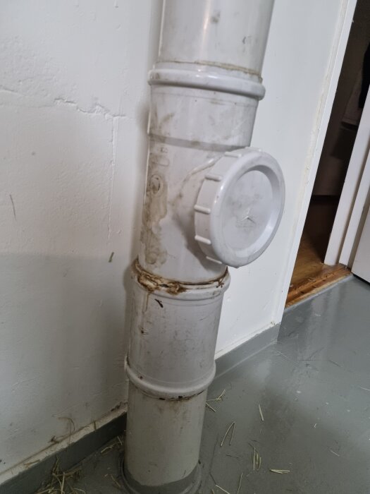 Avloppsrör i ett rum, delvis smutsigt och med tätning vid fogarna, med rund inspektionslucka.