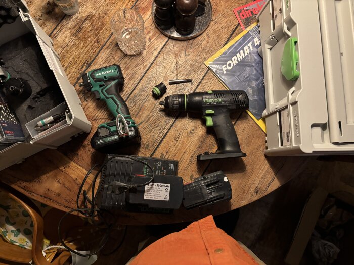 Verktyg på ett träbord: en HiKOKI-borrmaskin, en Festool-borrmaskin, en laddare och en öppen verktygslåda.