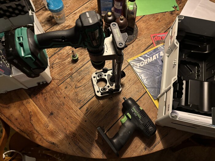 Verktygsbord med borrmaskin och andra byggverktyg, samt öppna förpackningar, på ett träbord.