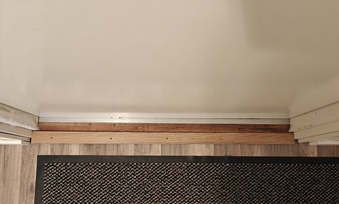 Golv med trälist vid dörr, ovanpå klinker. Skruvhål synliga i trälisten. Fundering kring att använda nivålist eller skarvlist i metall.